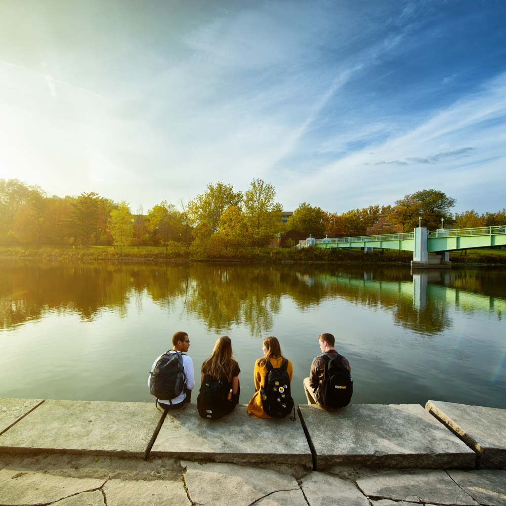 students sitting on the dock of river
